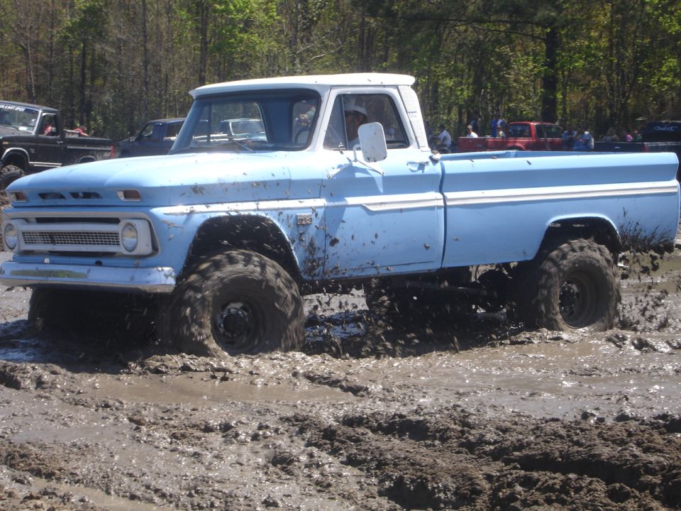Light blue pickup truck with white roof stuck in mud, lifted with large tires