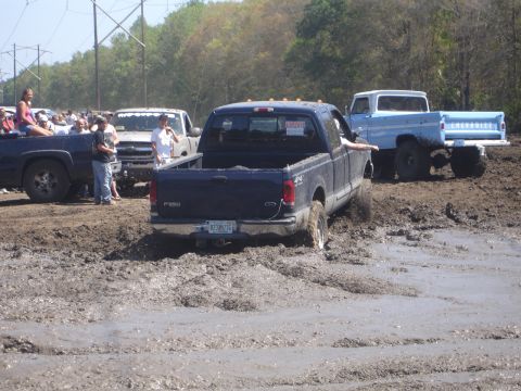 1989 Ford Bronco - A dark blue Ford F-250 pickup truck is stuck in the mud, with other vehicles and spectators in the background.