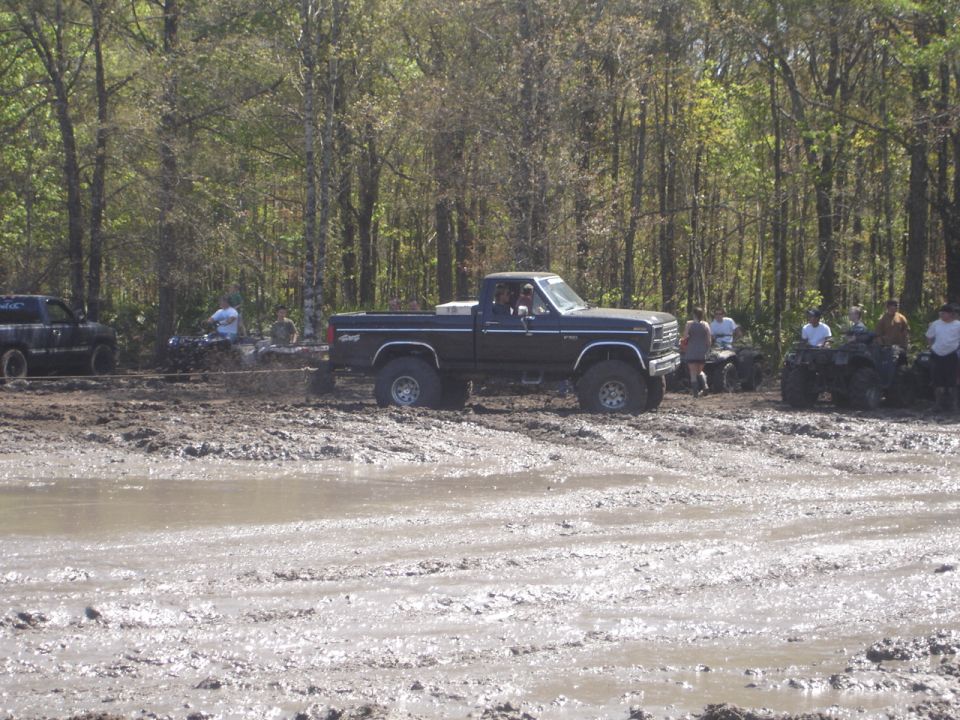 Ford pickup truck stuck in mud with people and ATVs around