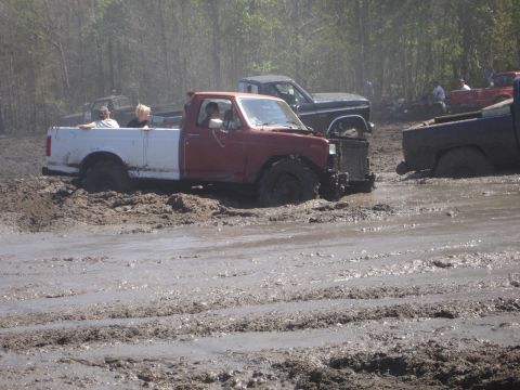 1989 Ford Bronco - Multiple trucks are stuck in a muddy area, with trees in the background.