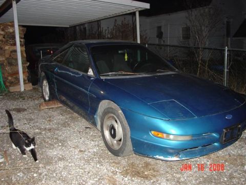 1993 Ford Probe - A blue 1993 Ford Probe is seen parked on gravel, with a cat in the foreground.