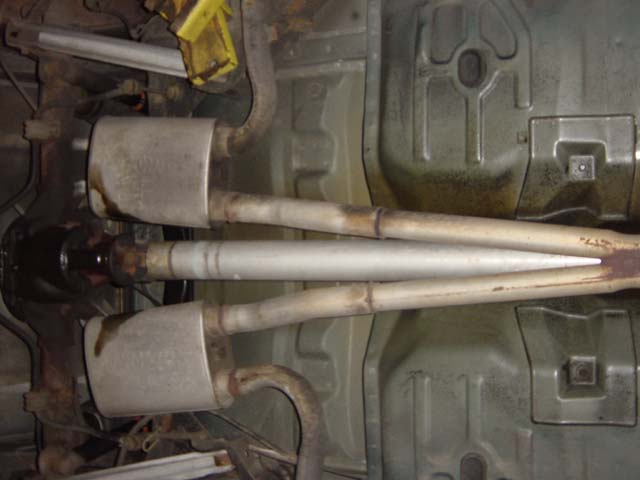 Underside of a vehicle showing dual exhaust mufflers, pipes and driveshaft