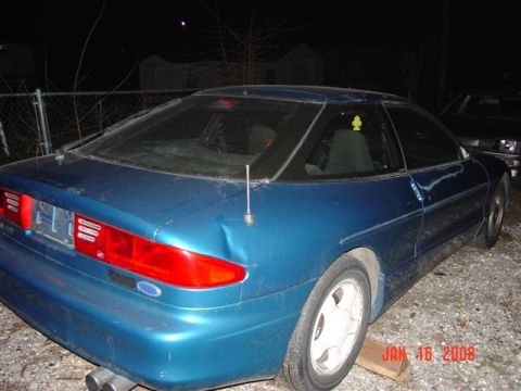1993 Ford Probe - The rear quarter panel of a blue 1993 Ford Probe is visible, parked next to another vehicle at night.