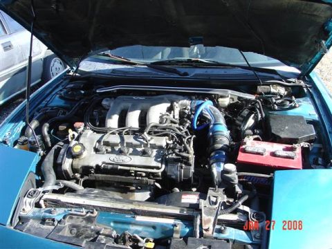1993 Ford Probe - Engine bay of a turquoise 1993 Ford Probe, a V6 engine and blue intake piping.