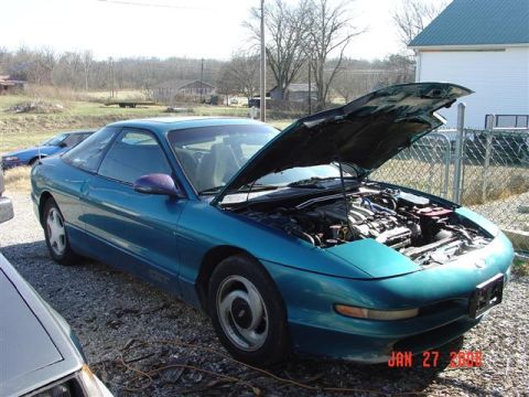 1993 Ford Probe - 1993 Ford Probe with its engine compartment exposed, parked outdoors next to other vehicles.