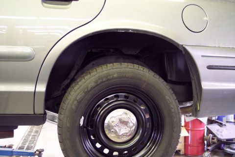 2001 Ford Crown Victoria - Rear wheel well of a 2001 Ford Crown Victoria, showing the silver body and black steel wheel.