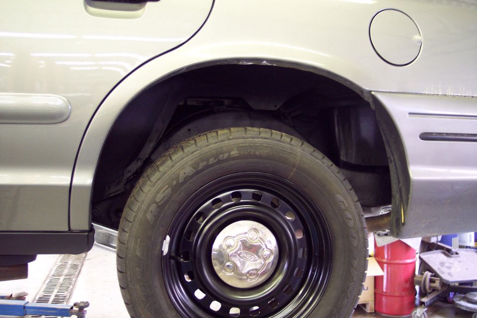 2001 Ford Crown Victoria rear wheel well and tire. Silver paint, black steel wheel with Ford center cap