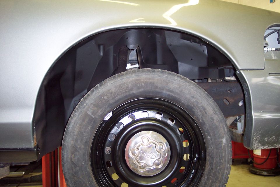 Close-up of the front wheel well of a 2001 Ford Crown Victoria, showing the tire and black steel wheel with a Ford hubcap