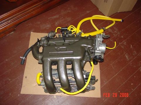 1993 Ford Probe - Engine intake manifold with yellow hoses is shown on a cardboard base on a wooden floor.