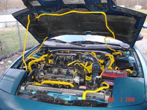 1993 Ford Probe - The engine bay is filled with yellow hoses, a prominent red battery, and other engine components.