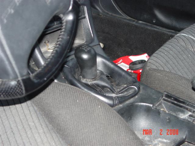 Manual shifter and handbrake on a console with trim removed, grey cloth seats