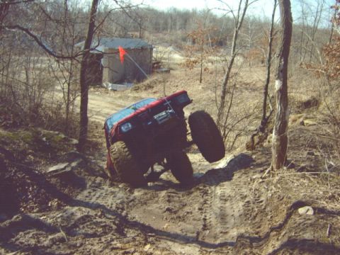 1992 Ford Bronco - Off-road vehicle stuck in muddy terrain with trees and a building visible.