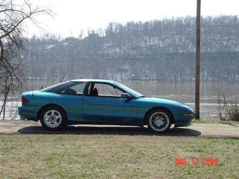 1993 Ford Probe - A teal 1993 Ford Probe GT is parked by a river on a clear day.