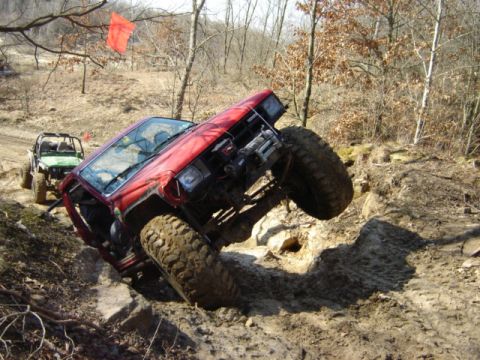 1992 Ford Bronco - Two off-road vehicles navigate a challenging rocky trail in a wooded area.