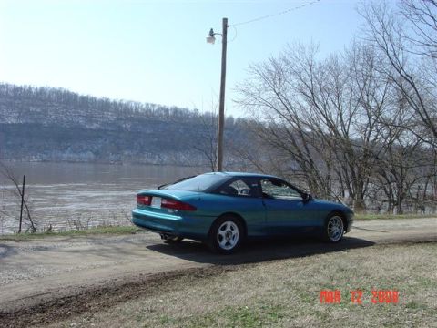 1993 Ford Probe - A teal 1993 Ford Probe is parked on a dirt road next to a wide river under a clear sky.