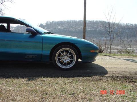 1993 Ford Probe - A teal 1993 Ford Probe GT is seen from the side on a dirt road with a wooded hill in the background.