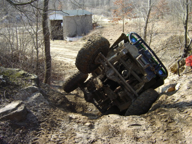 Off-road vehicle tipped on its side in a muddy ditch. The front grille and headlights are visible