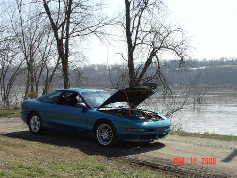 1993 Ford Probe - A teal 1993 Ford Probe is parked by a river with its hood up, showing the engine bay.