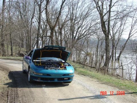 1993 Ford Probe - A teal 1993 Ford Probe sits on a dirt road with its hood open, adjacent to a river that has flooded its banks.