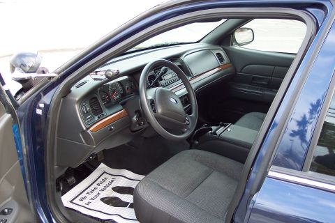 2001 Ford Crown Victoria - The interior of a dark blue police car is visible, showing the dashboard, steering wheel, and seats.