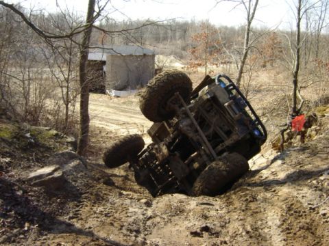 1992 Ford Bronco - An overturned off-road vehicle lies on its side in a muddy, wooded area.