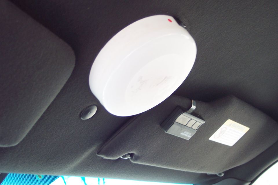 Car ceiling with a white dome light and a garage door opener attached to the visor