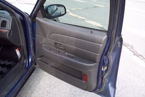 2001 Ford Crown Victoria - Interior view of a blue car's door panel and dashboard, showing the driver's side controls.