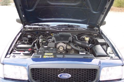 2001 Ford Crown Victoria - Engine bay of a blue 2001 Ford Crown Victoria, showing the V8 engine and front grille with Ford emblem.