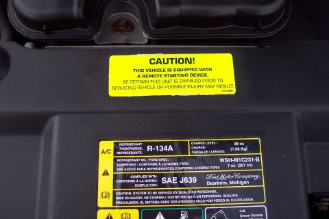 2001 Ford Crown Victoria - Vehicle maintenance labels in the engine bay detail refrigerant type and charge level, along with a caution about remote start systems.