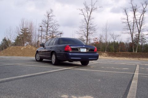 2001 Ford Crown Victoria - Rear view of a dark blue 2001 Ford Crown Victoria parked in an empty lot under a cloudy sky.