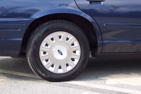 2001 Ford Crown Victoria - Close-up of a blue sedan's rear wheel, a Ford hubcap and tire.