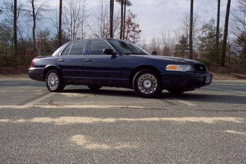 2001 Ford Crown Victoria - A dark blue sedan is parked on an asphalt surface with trees in the background.