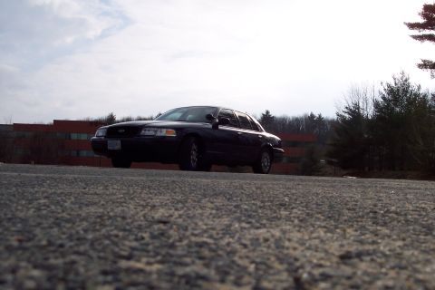 2001 Ford Crown Victoria - A black 2001 Ford Crown Victoria is parked on an asphalt surface with a building and trees in the background.