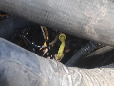 1989 Ford Bronco - Close-up view of engine components, including a yellow dipstick and a black hose, within the engine bay.