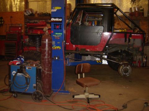 1992 Ford Bronco - A red Jeep Wrangler is elevated on a lift in a workshop, surrounded by tools and equipment.