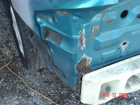 1993 Ford Probe - The rear quarter panel of a teal 1993 Ford Probe exhibits significant rust and damage, with a white bumper visible.