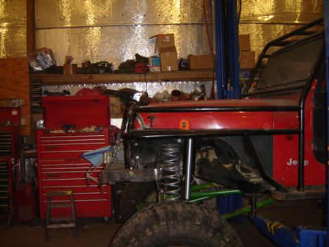 1992 Ford Bronco - A red Jeep Wrangler is shown on a lift inside a workshop, with tools and storage visible.