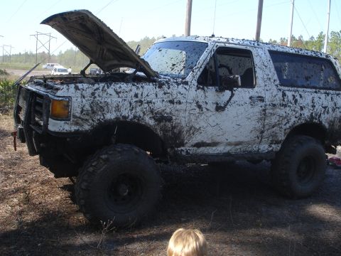 1989 Ford Bronco - This white SUV is heavily coated in mud, with its hood propped open after an off-road excursion.