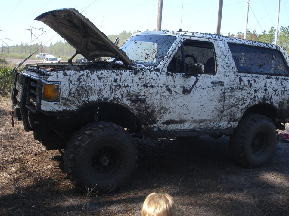 White SUV covered in mud, hood open, parked off-road