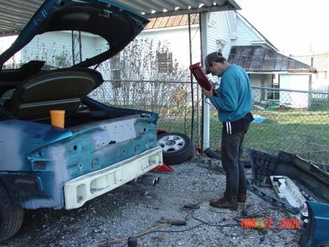 1993 Ford Probe - Man works on the rear bumper of a 1993 Ford Probe, which is undergoing bodywork.