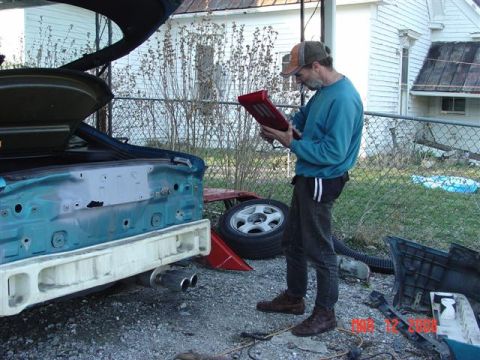 1993 Ford Probe - A man examines a red component while standing next to the disassembled rear of a car.