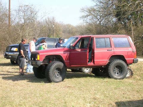 1996 Ford Bronco - A red Jeep Cherokee is parked outdoors with its driver's door open, alongside another vehicle.