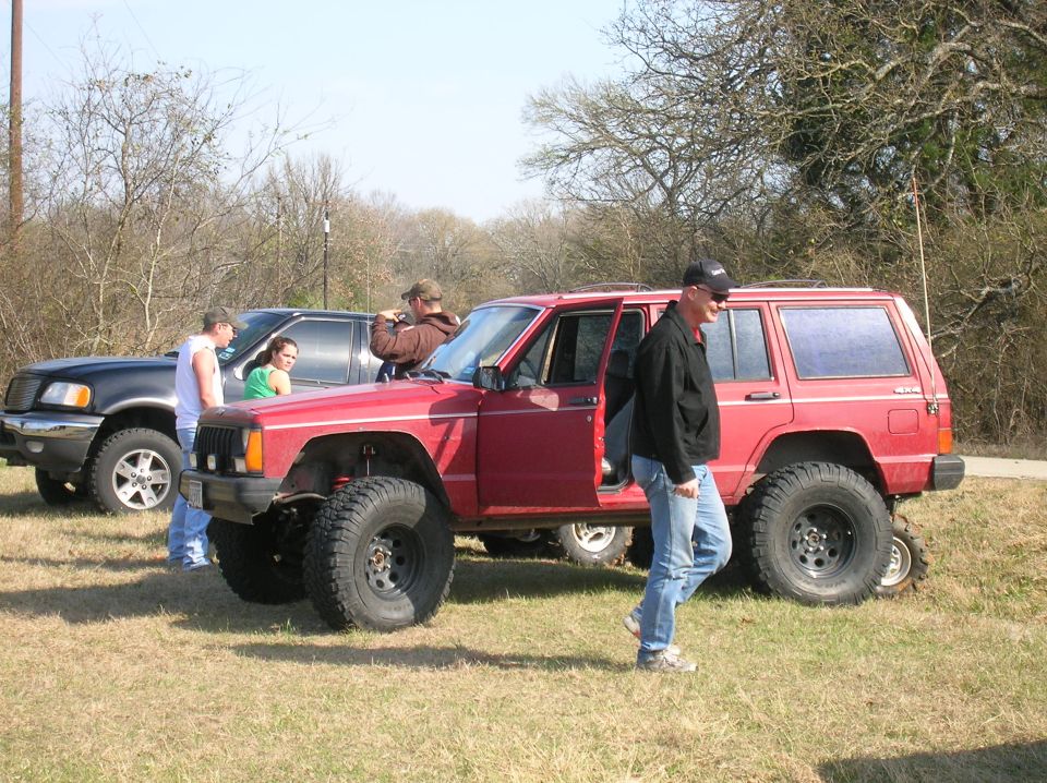 Red Jeep Cherokee with lifted suspension and off-road tires parked next to a black pickup truck