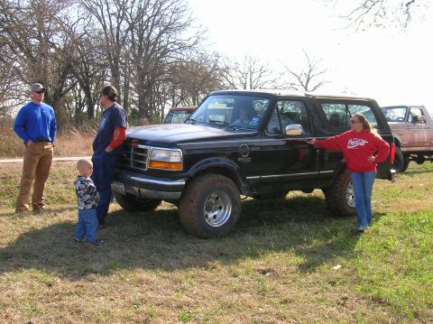 1996 Ford Bronco - Black 1996 Ford Bronco with people gathered around it in a field.