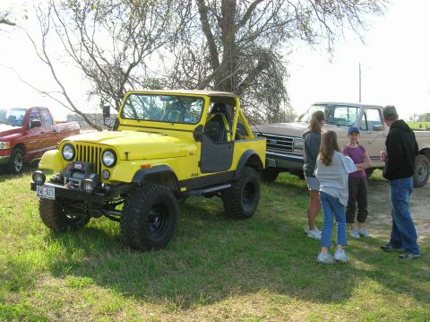 1996 Ford Bronco - A yellow Jeep CJ and a tan Ford pickup truck are parked on a grassy area with trees overhead.