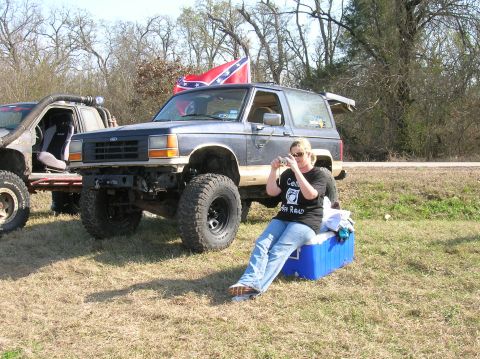 1996 Ford Bronco - A woman sits on a cooler in front of a modified Ford Bronco, which has a Confederate flag flying from its roof.
