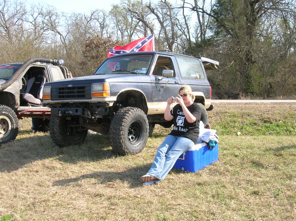 Dark blue Ford Bronco with lifted suspension and off-road tires, parked on grass next to another off-road vehicle