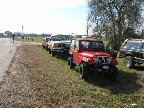 1996 Ford Bronco - Multiple off-road vehicles are parked in a line on the side of a road.