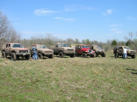 1996 Ford Bronco - Several modified trucks and SUVs are gathered in an open field on a sunny day.