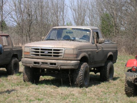 1996 Ford Bronco - A muddy Ford Bronco is parked in a field with other vehicles nearby.